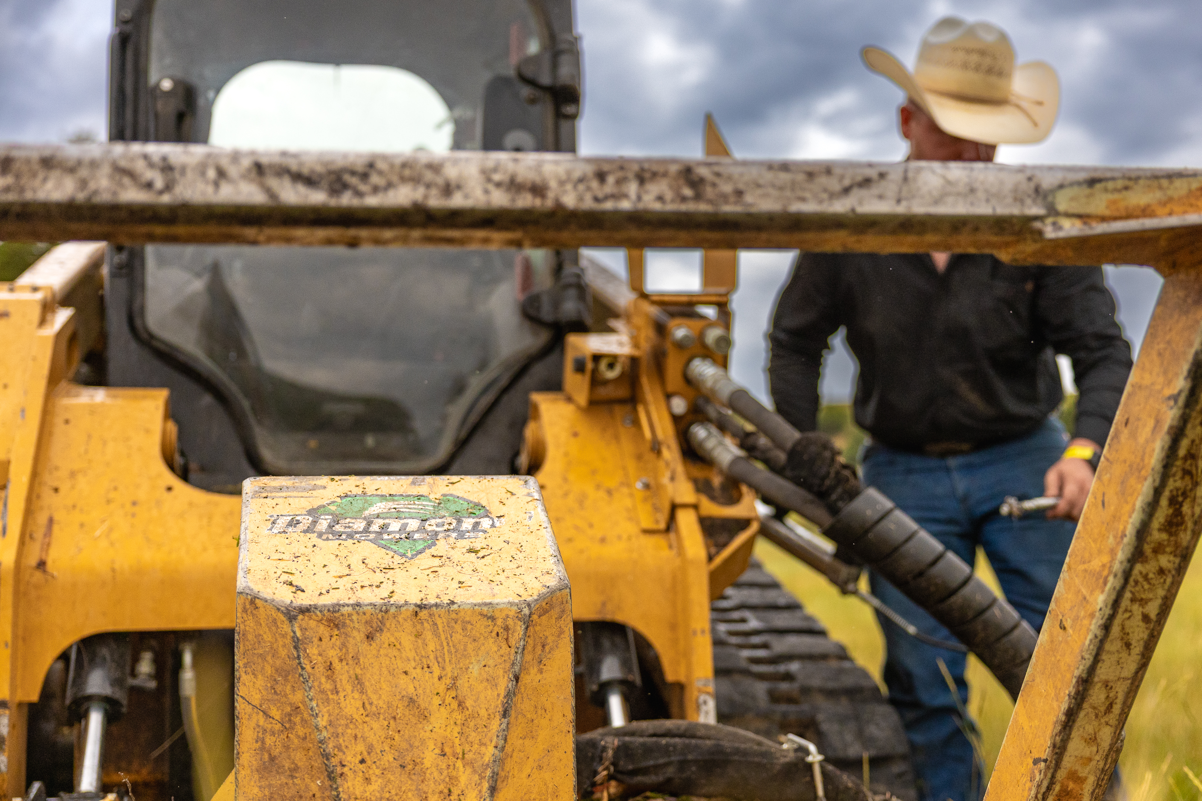 person standing next to a skid steer with a disc mulcher attached